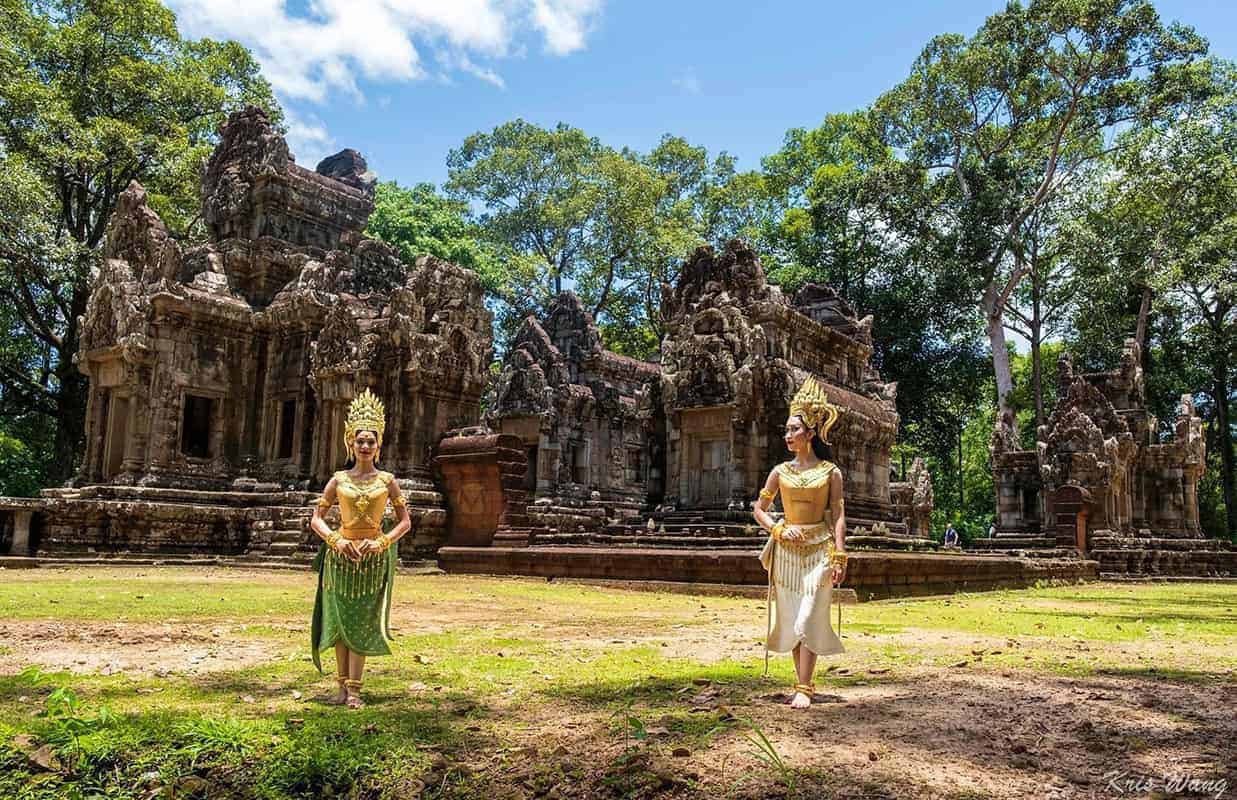 Two traditional dancers in front of an ancient temple surrounded by lush greenery.