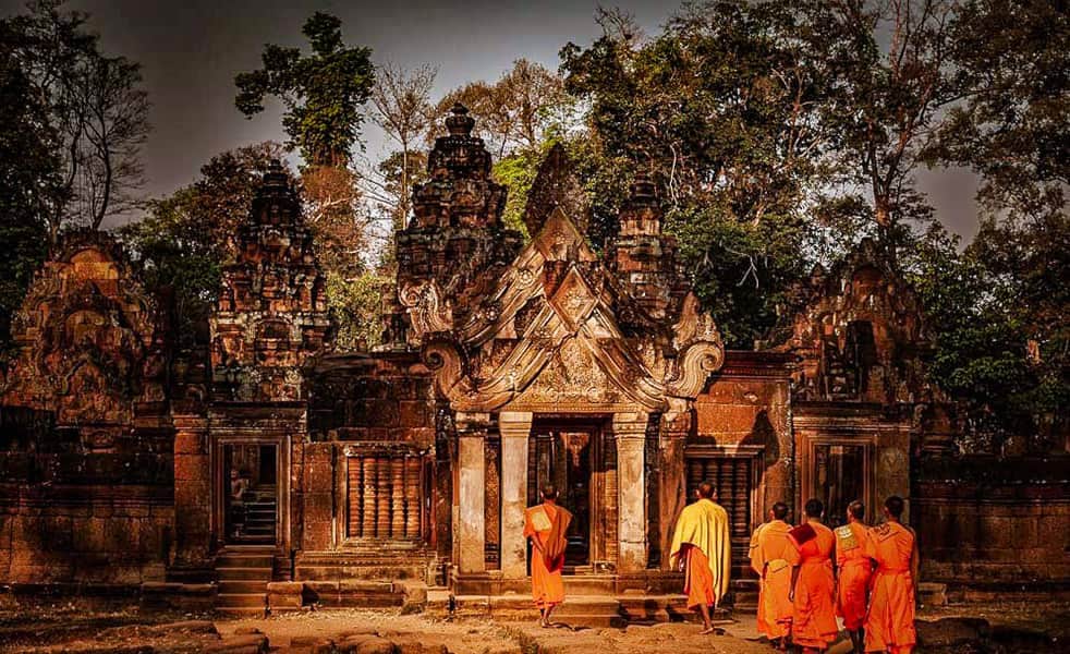 Khmer temple ruins with monks in orange robes at sunset.