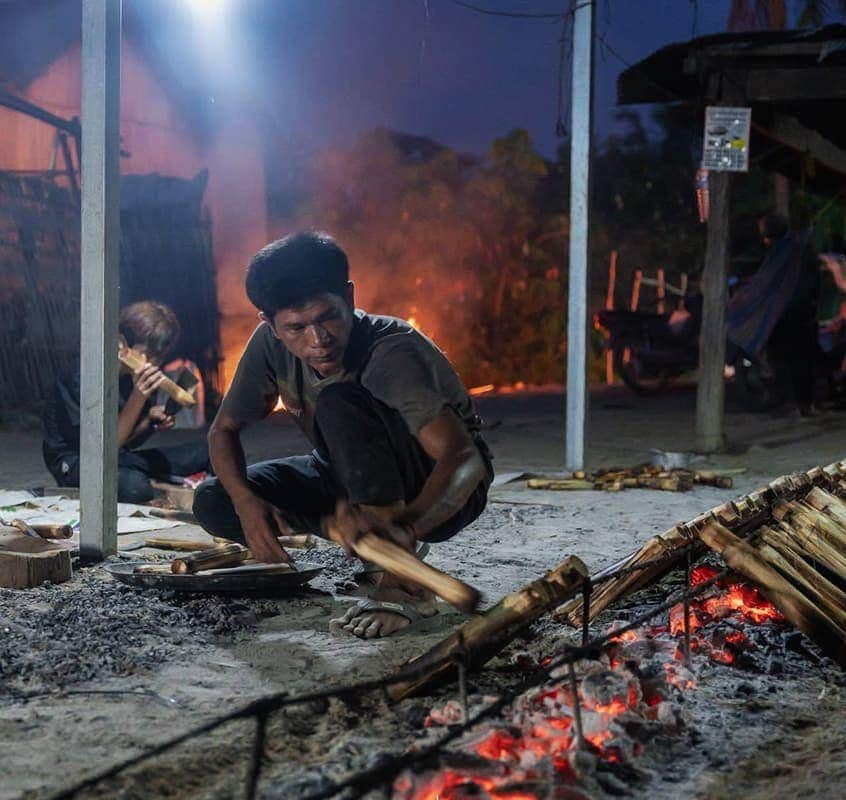 Child cooking food over an open fire outdoors.