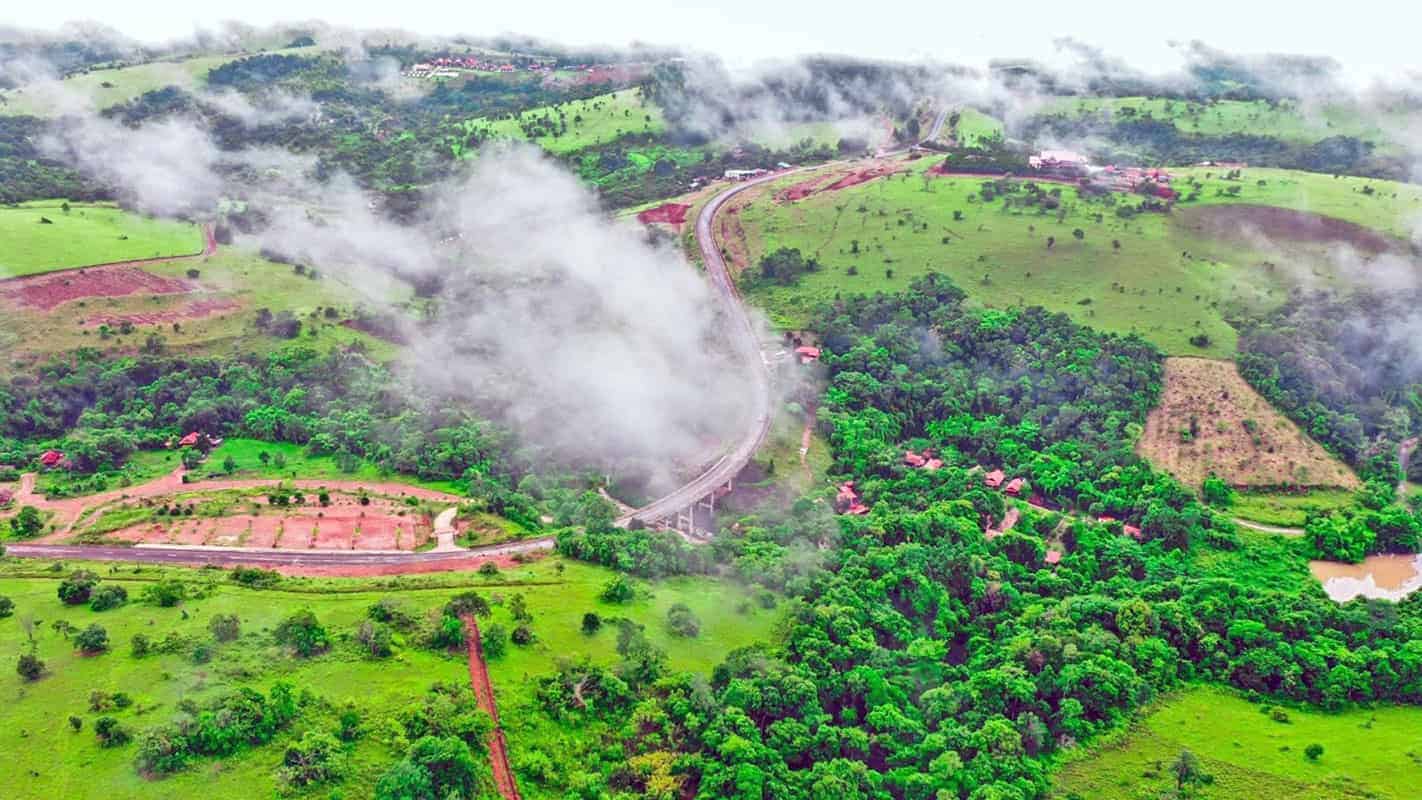 Aerial view of lush green hills with winding roads and misty clouds in a vibrant landscape.
