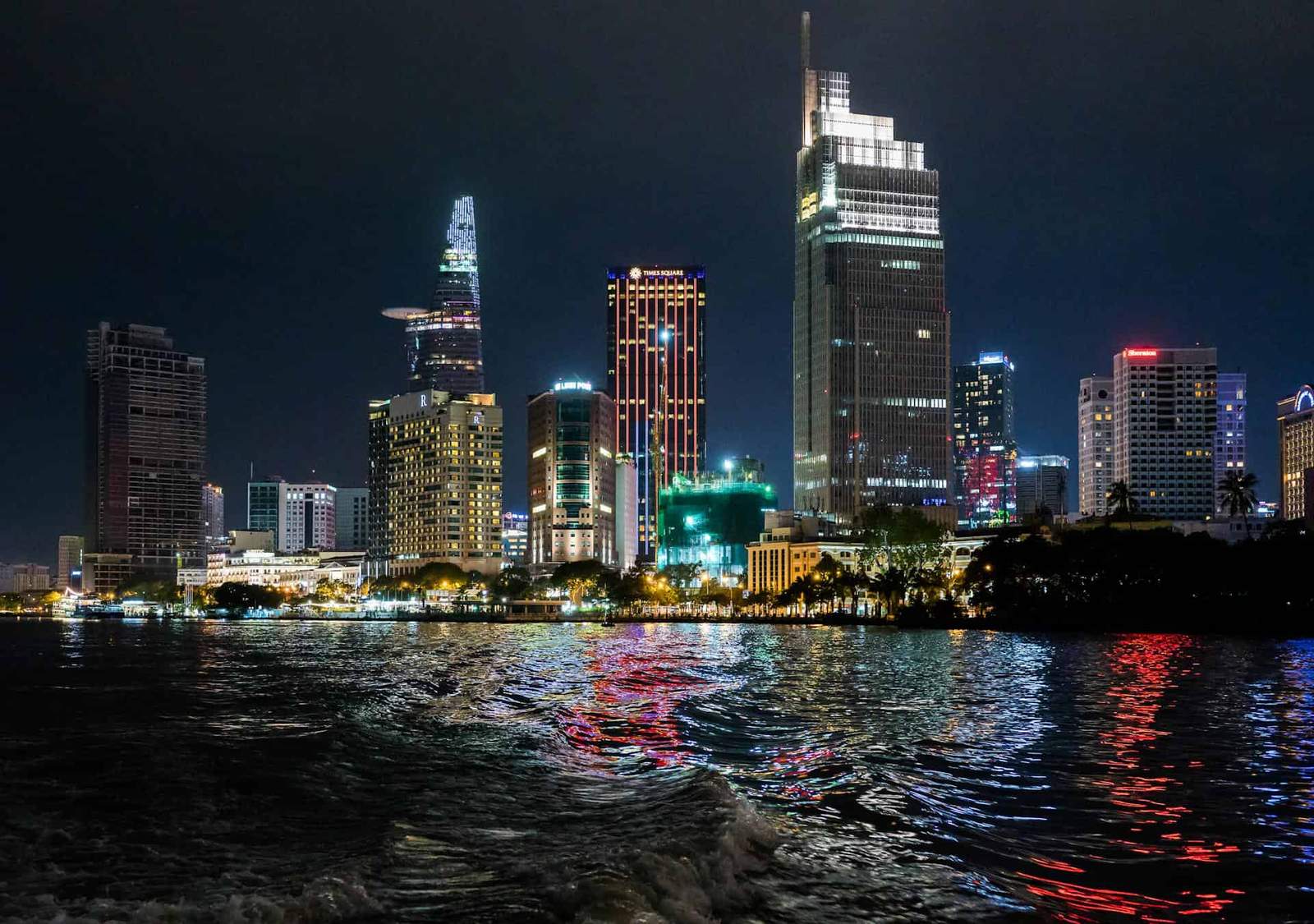 Ho Chi Minh City skyline at night with illuminated skyscrapers and reflections on the water.