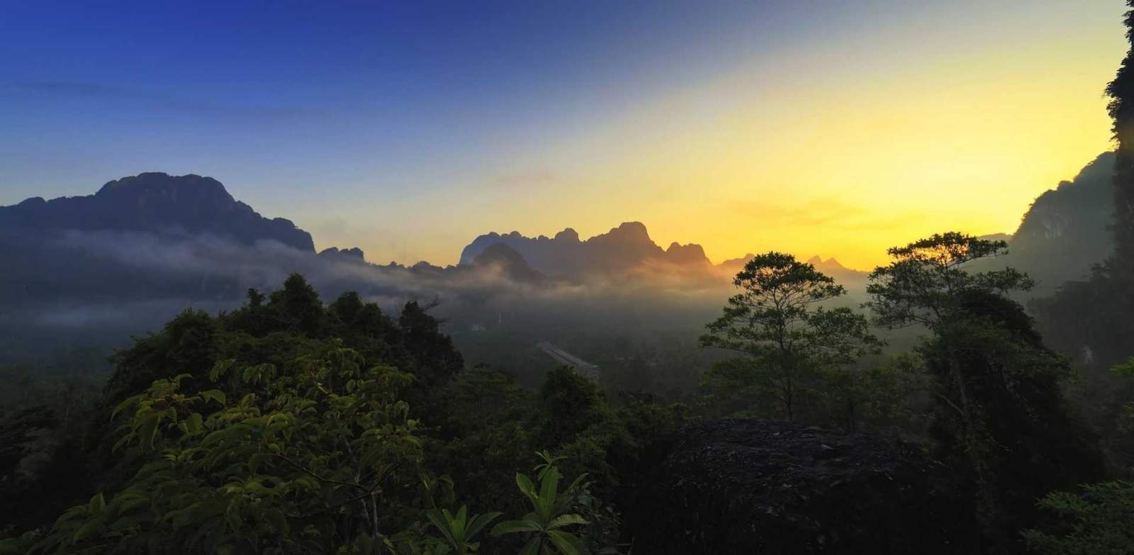 Scenic tropical mountain landscape at sunset with lush greenery and vibrant sky.