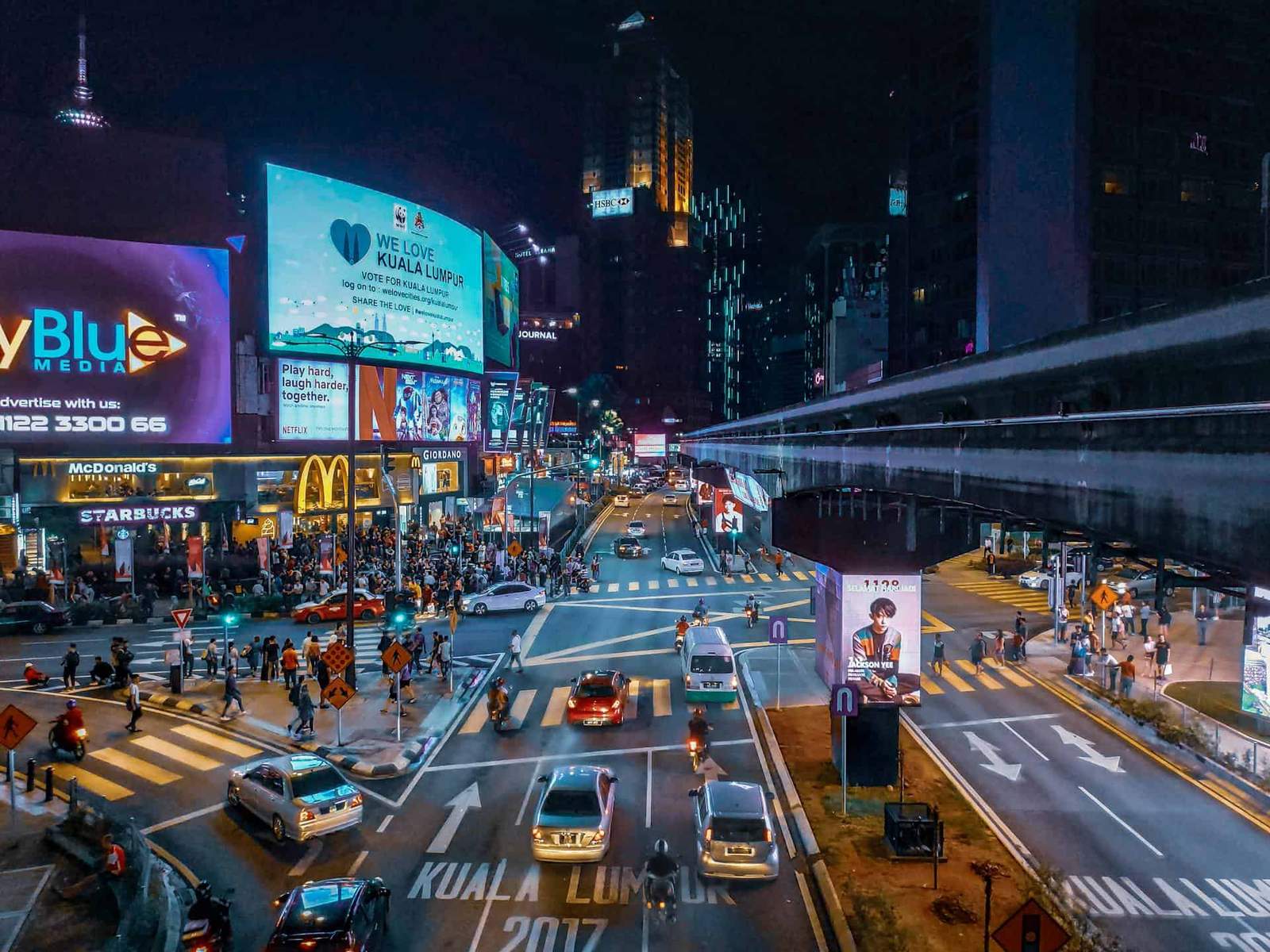 Night view of Kuala Lumpur city with busy streets and illuminated billboards.