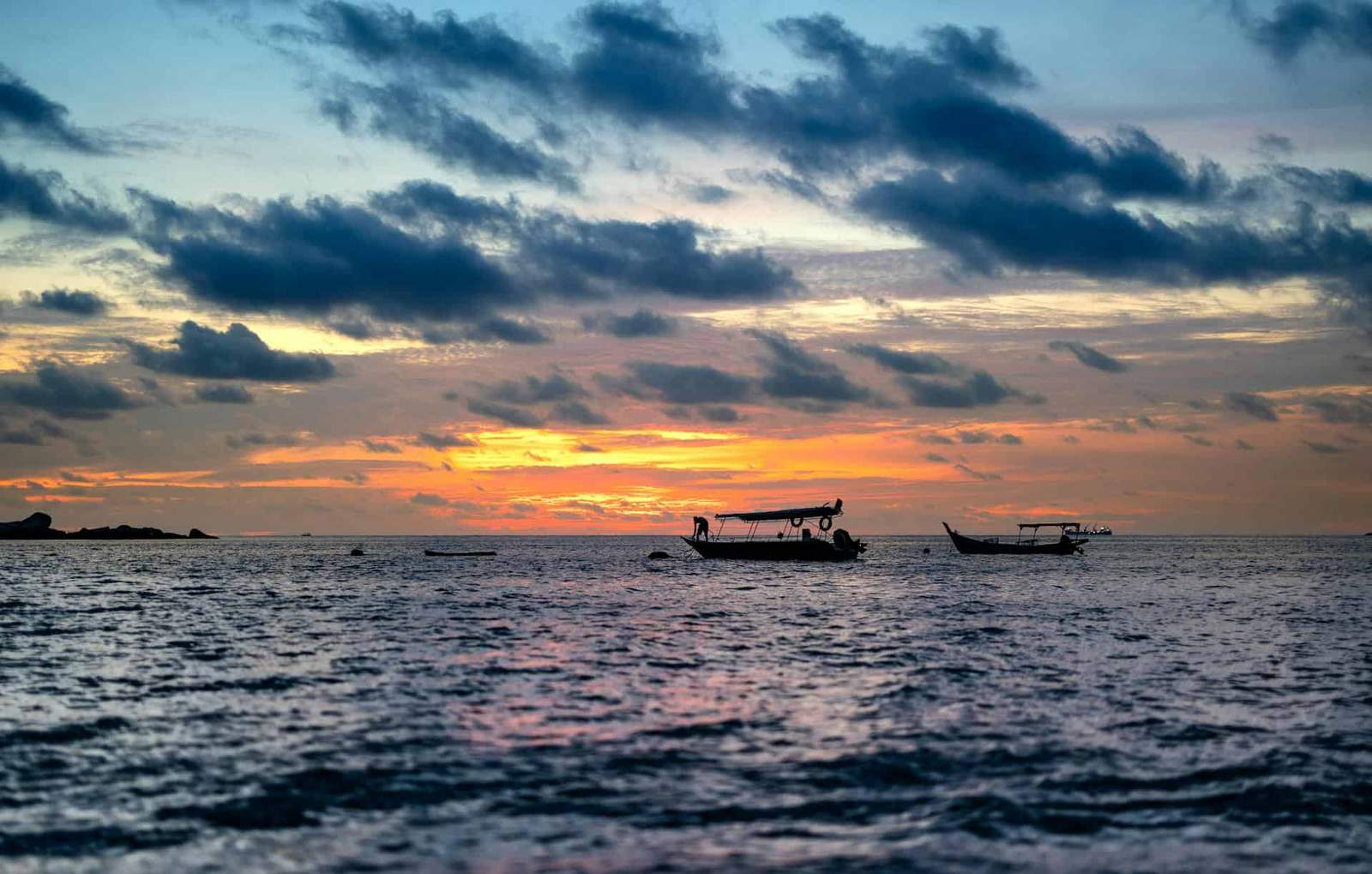 Beautiful sunset over calm Malaysian waters with boats at dusk.