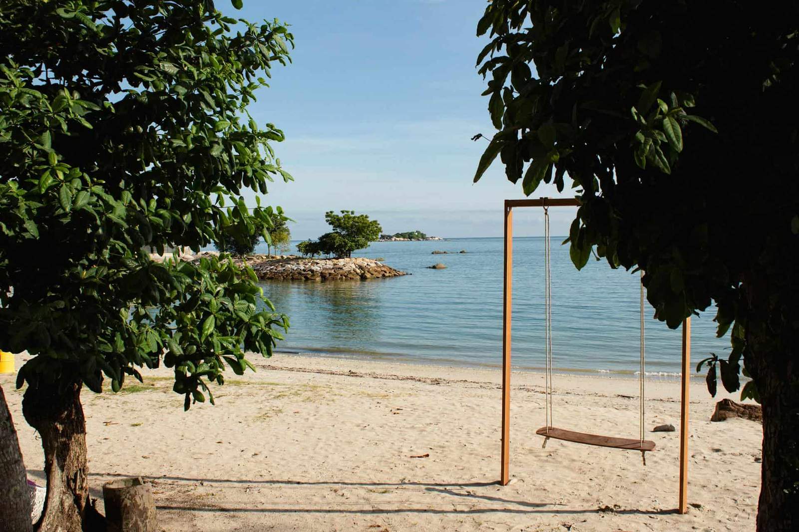 Beach swing overlooking calm ocean waters and sandy shoreline.