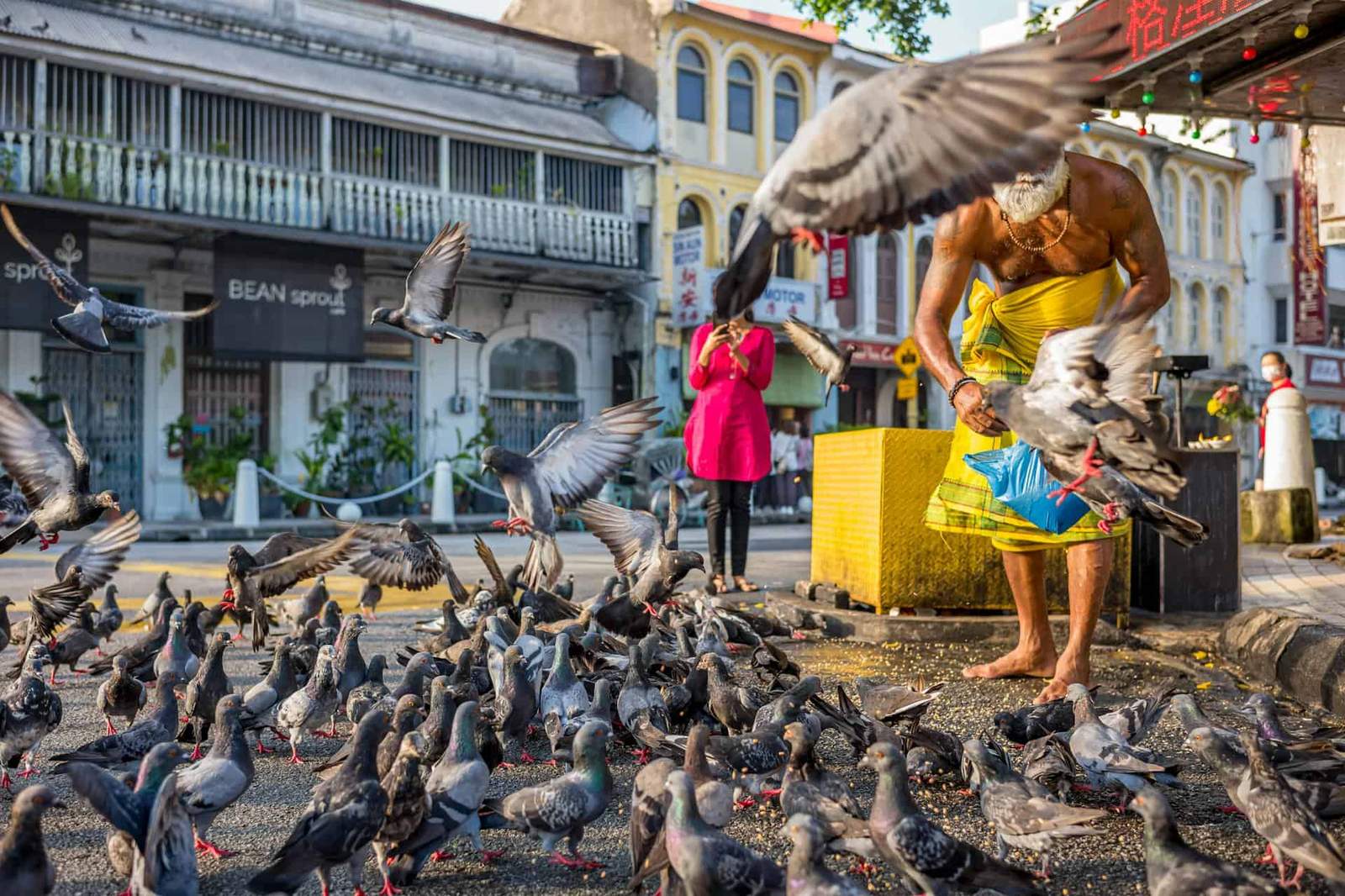 Man feeding pigeons on a busy street in Asia, vibrant city scene.
