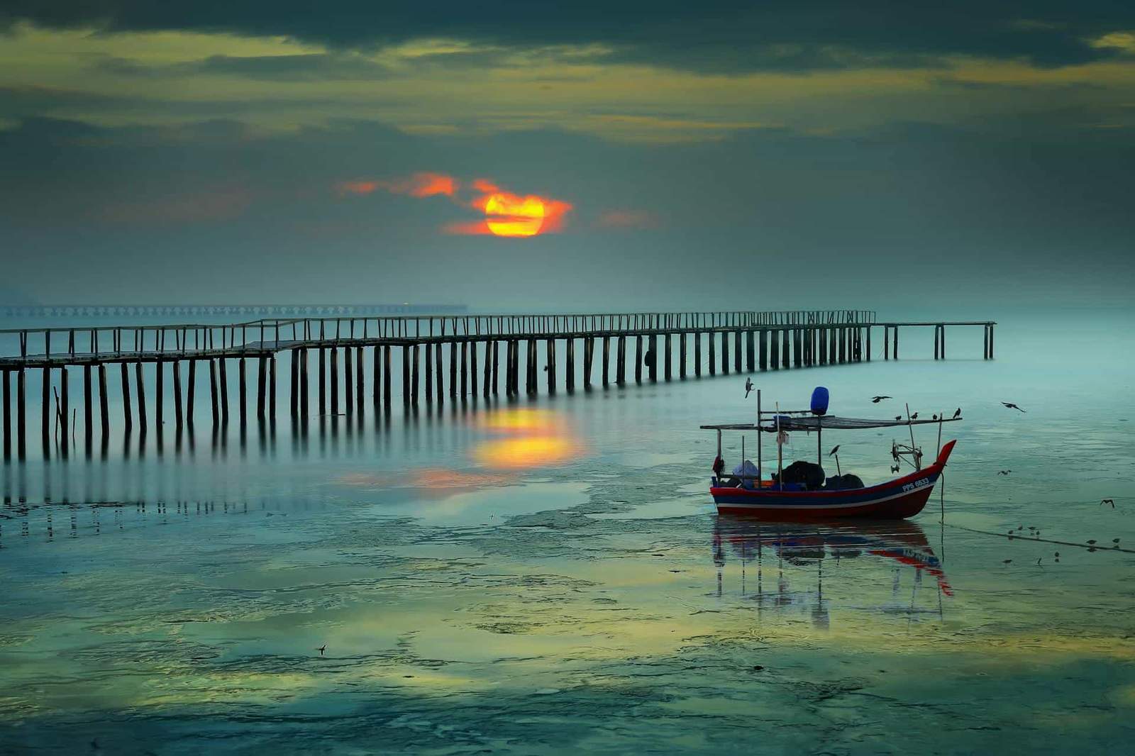 Sunset over pier and boat at the beach.
