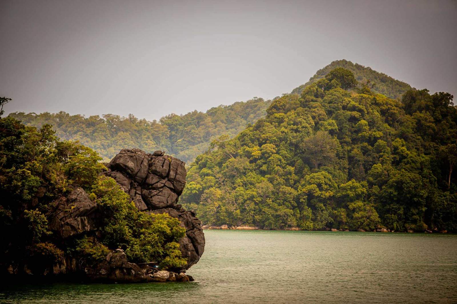 Scenic mountain lake with lush green trees and rocky shoreline in a tropical setting.