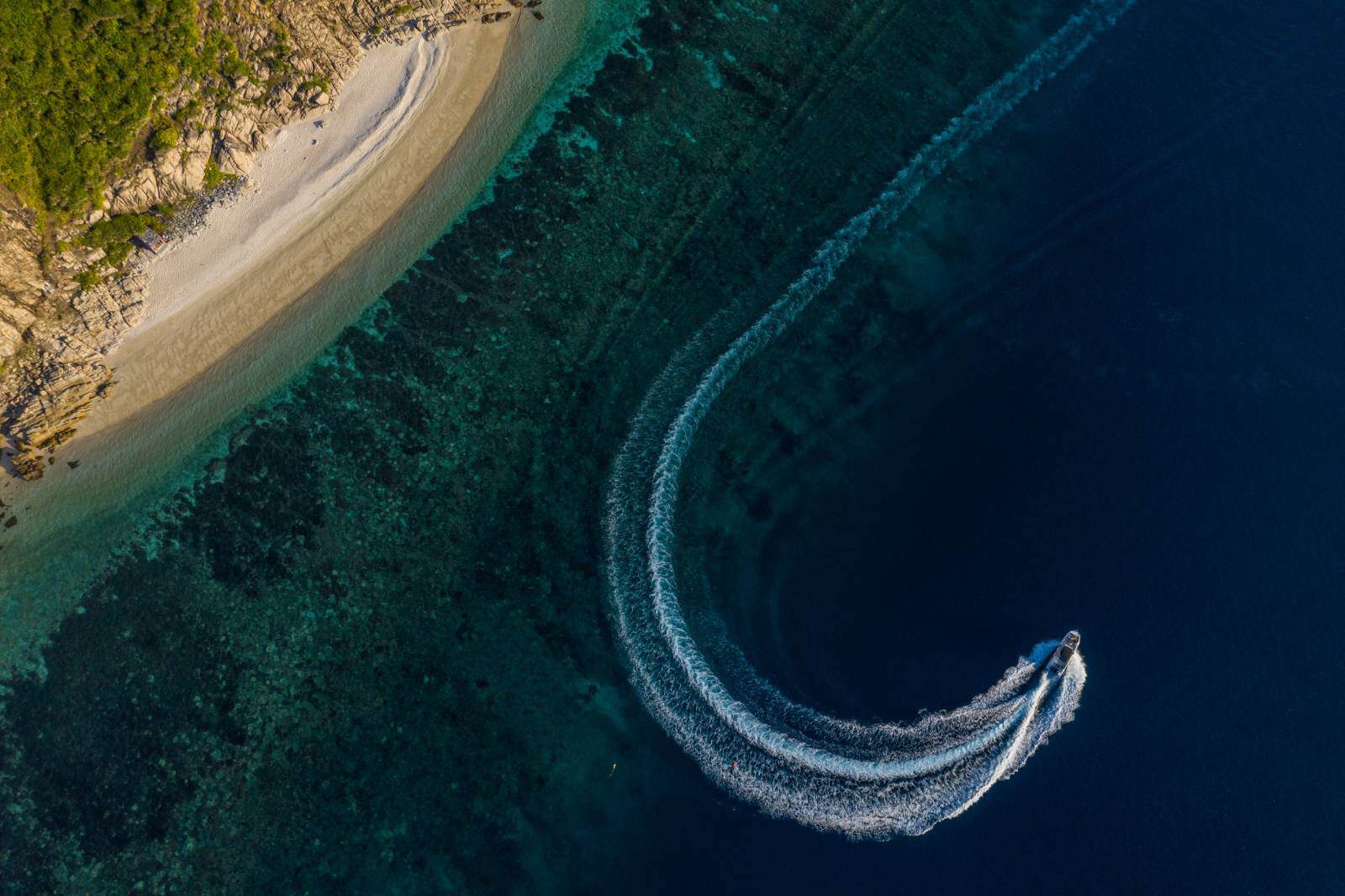 Boat cruising along clear blue waters near a scenic shoreline.