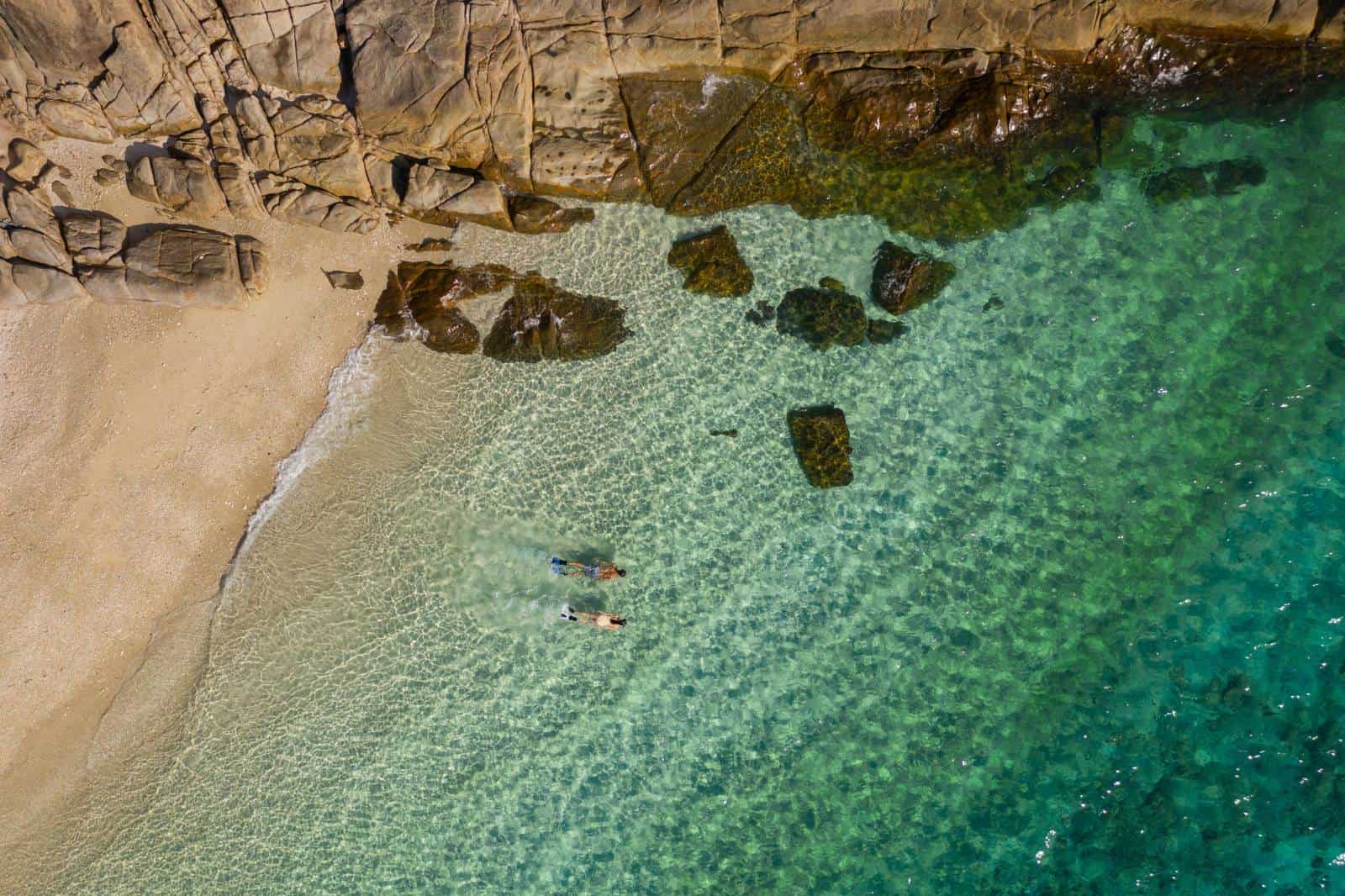 Aerial view of a tropical beach with clear turquoise water and rocky shoreline.