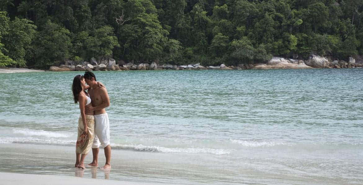 Couple enjoying a romantic moment on a tropical beach with clear waters and lush greenery in the bac.