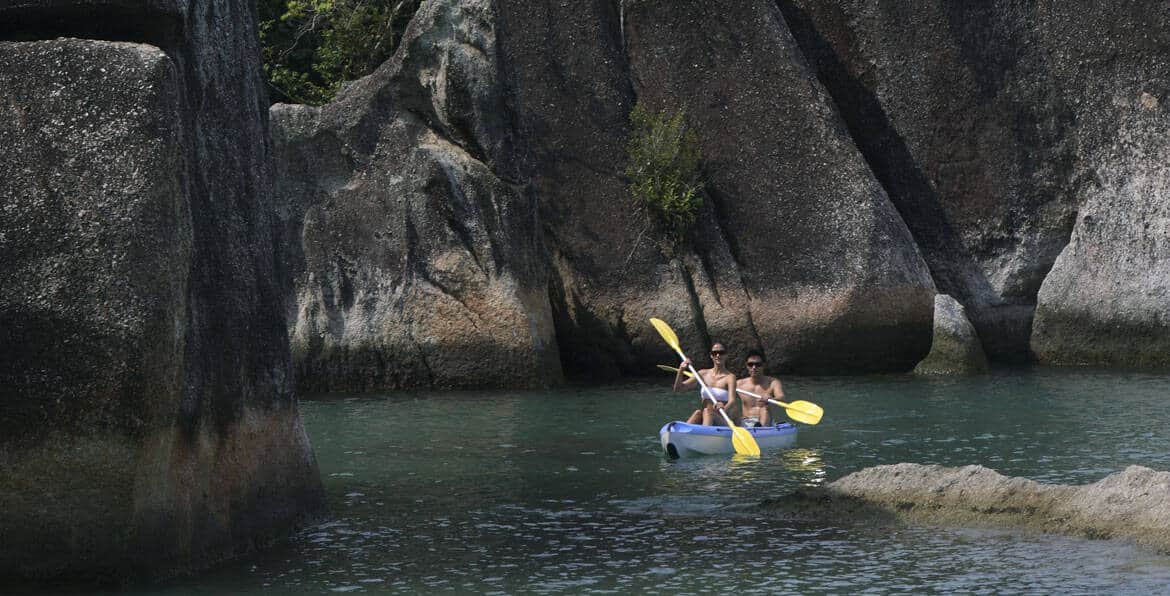 Kayakers paddling through scenic river canyon with large rocks and lush greenery.