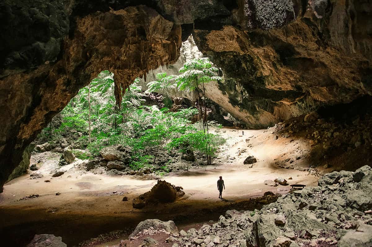 Hua Hin cave with lush greenery and a lone traveler exploring the natural rock formations.