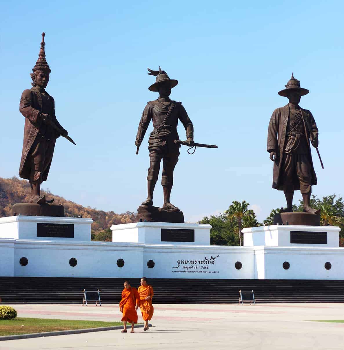 Three large statues of Thai historical figures with monks walking nearby in Thailand.