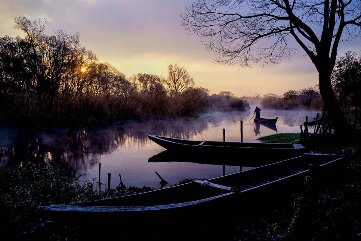 Serene river scene with boats and mist at sunrise, perfect for travel and nature exploration.