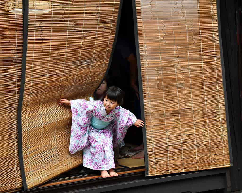 Child in traditional kimono peeking out of a wooden house.